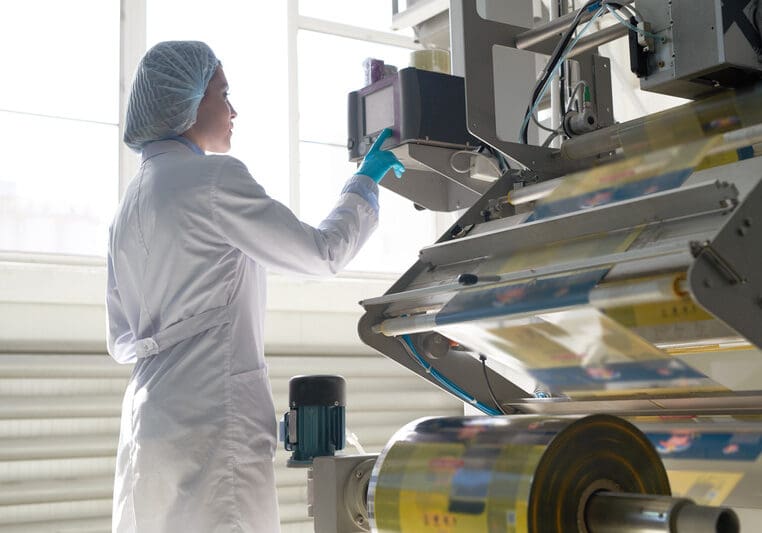 Side view portrait of female factory worker wearing clean white coat standing by machine units at packaging line, copy space